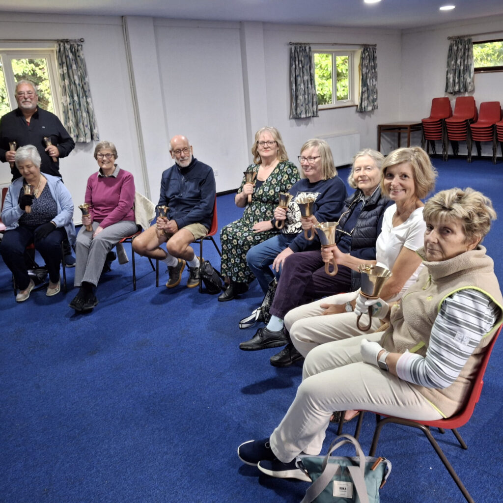 The froup of handbell ringers sitting in a semi circle